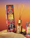 a glasshouse Dusk at the Kashubh diffuser, which is a decorative glass diffuser with a golden base and a collection of wooden sticks. The diffuser is placed on a sandy surface, and there is a box of the Dusk at the Kashubh diffuser next to it.