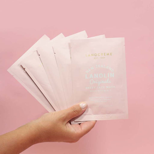 A hand holding a packet of Lanolin Original Sheet Face Mask against a pink background.