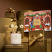 a collection of holiday-themed items, including a candle, gift boxes, and a gingerbread house illustration, all set against a gold background.