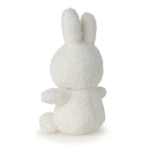 A white, fluffy stuffed bunny toy is sitting on its back with its arms outstretched.