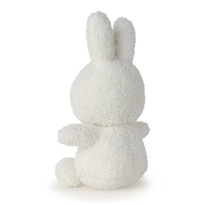 A white, fluffy stuffed bunny toy is sitting on its back with its arms outstretched.