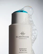 A bottle of Glasshouse Fragrances shampoo with a blue cap, surrounded by bubbles, with the label reading "Midnight in Milan Saffron & Rose".