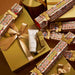 a collection of golden gift boxes and packages adorned with festive designs, including Christmas-themed patterns and ribbons.